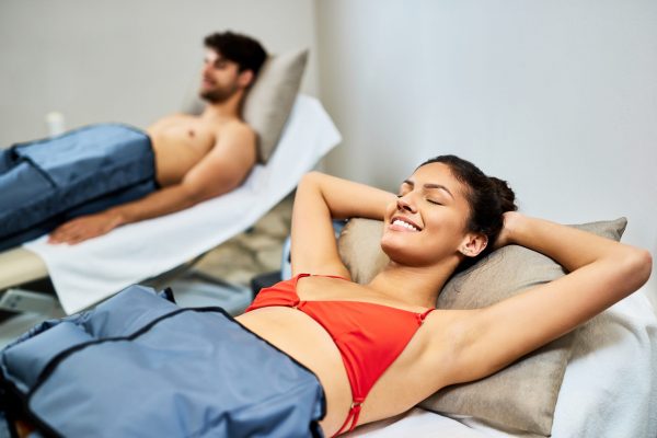 Young couple relaxing during pressotherapy at the spa. Focus is on happy woman.